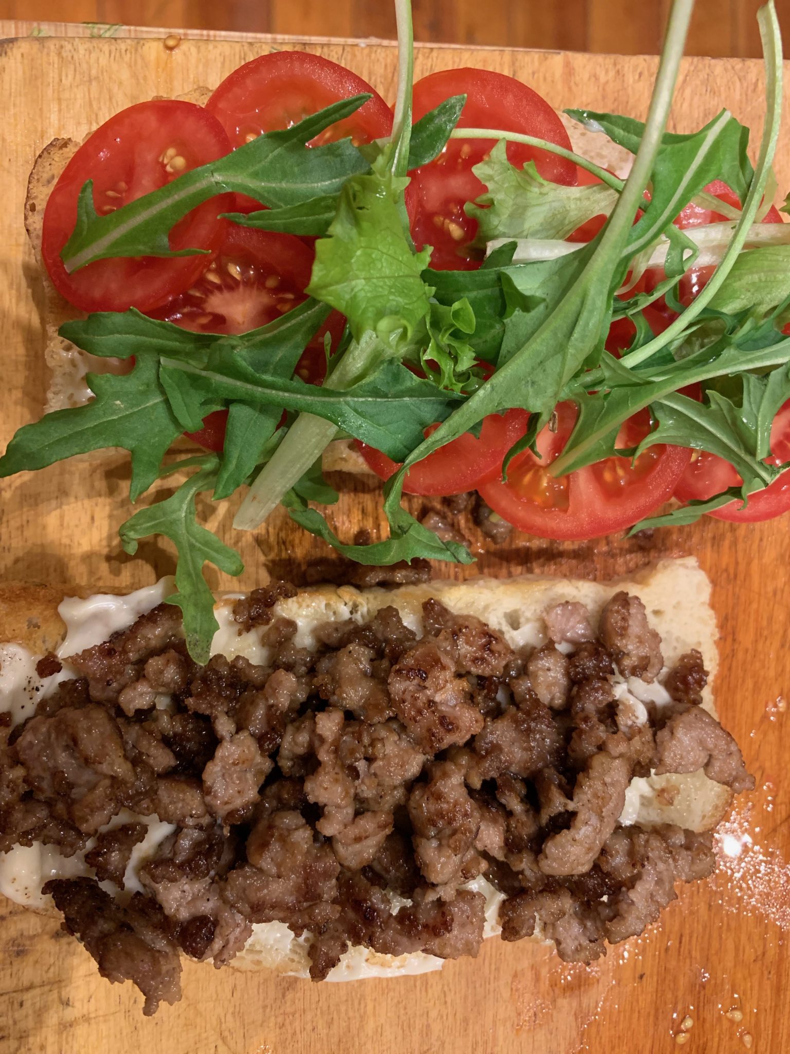 two slices of bread topped with ground pork, tomato and arugula