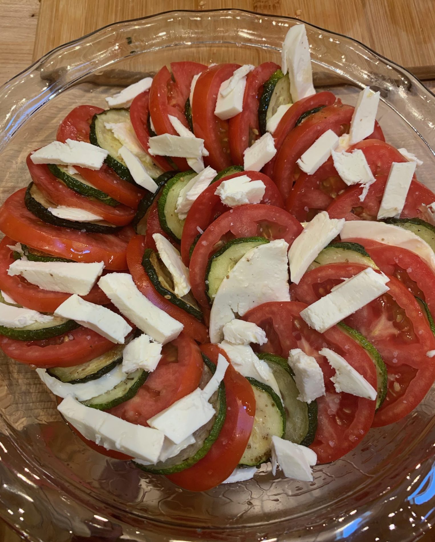 Slices of zucchini, tomato and mozzarella are layers in a glass pie plate before baking