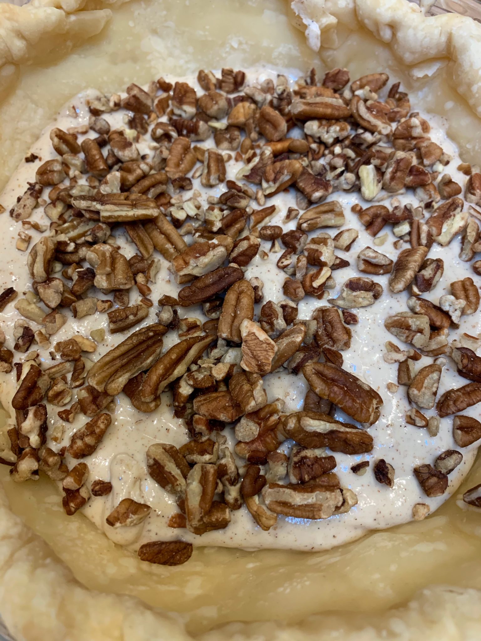 Showing chopped pecans layered on top of the cheesecake so as not to disturb the filling
